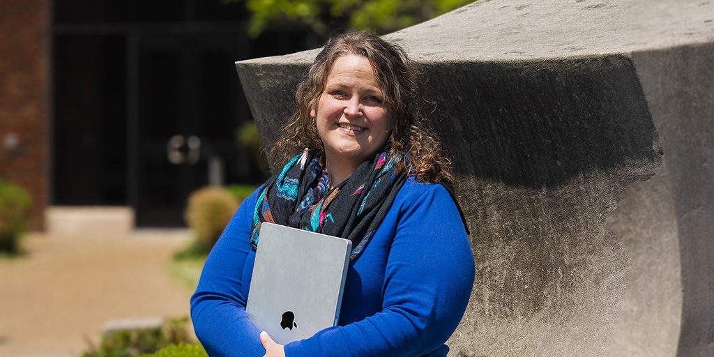 Rebekah Dement holding laptop sitting outside on IU Southeast campus