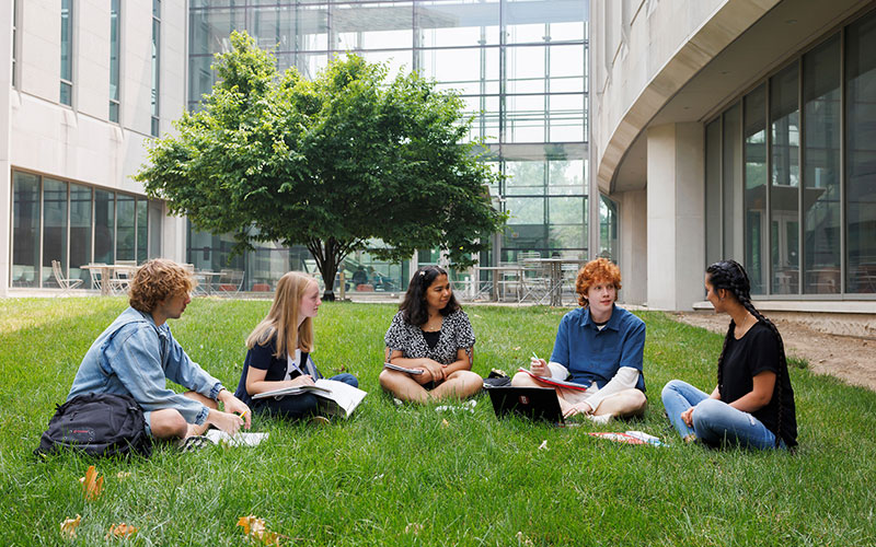 Students studying together while sitting on the grass outside an IU Bloomington campus building