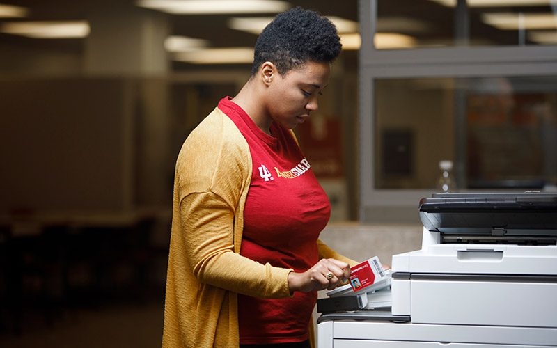 A woman stands at a printer.